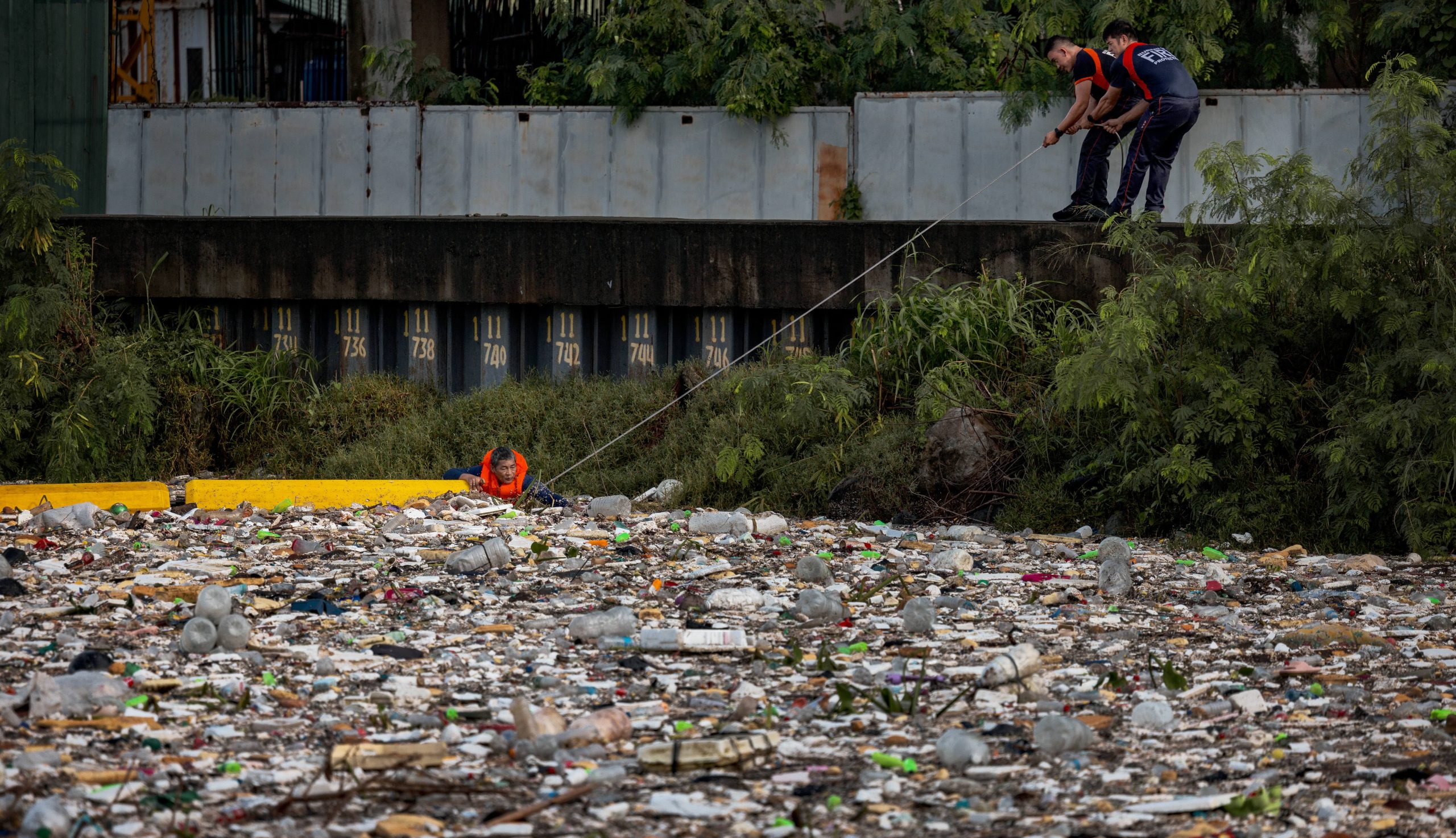 Workers pull on a plastic boom as they remove garbage that is clogging a river amid heavy rain on August 12, 2026 in Paranaque, Metro Manila, Philippines. (