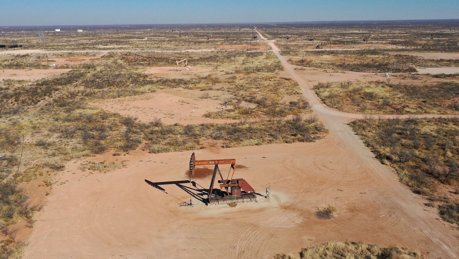 a large piece of orange equiptment seen sitting on the sand from an aerial view with a scrubbing green landscape stretching out for miles towards the horizon line — Image via Grist