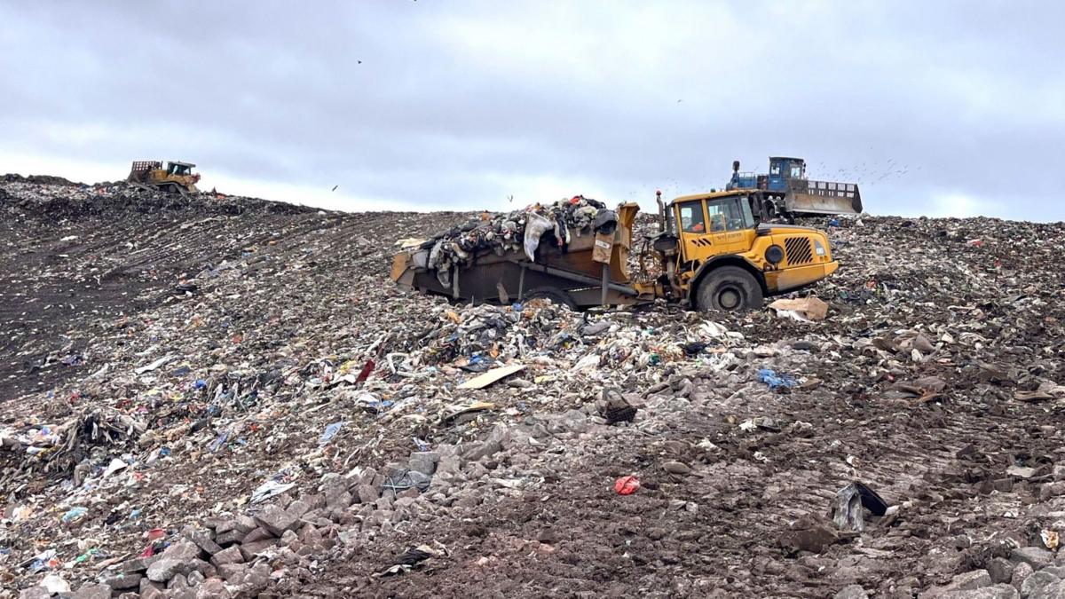 A landfill site with rubbish on the ground and machines pushing it into place.