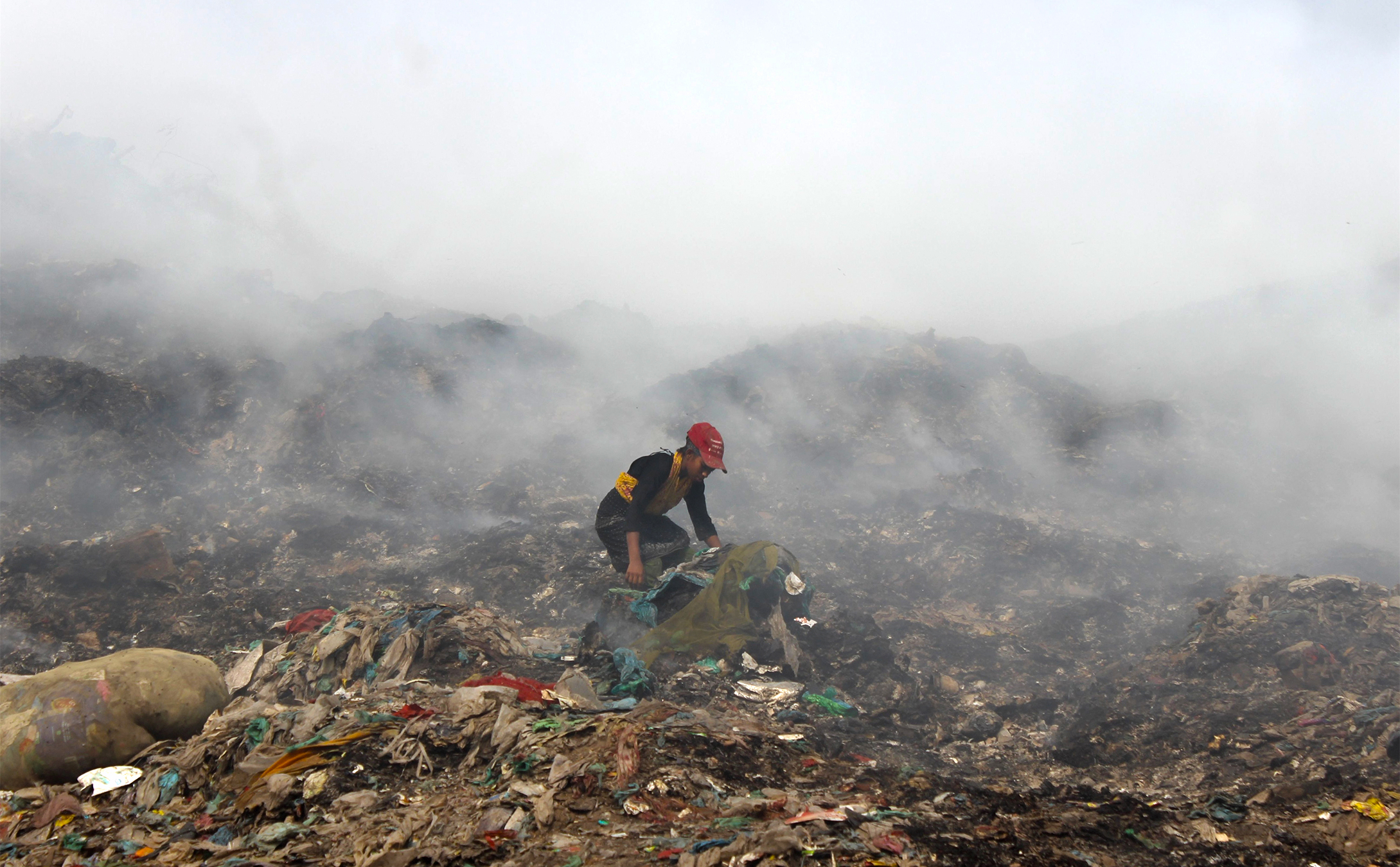 A waste picker works amid thick smoke rising from the vast garbage mounds at Dhaka North City Corporation’s Aminbazar landfill in Savar. She was looking for plastic or other valuable recyclable items. Image by Md Jahidul Islam.