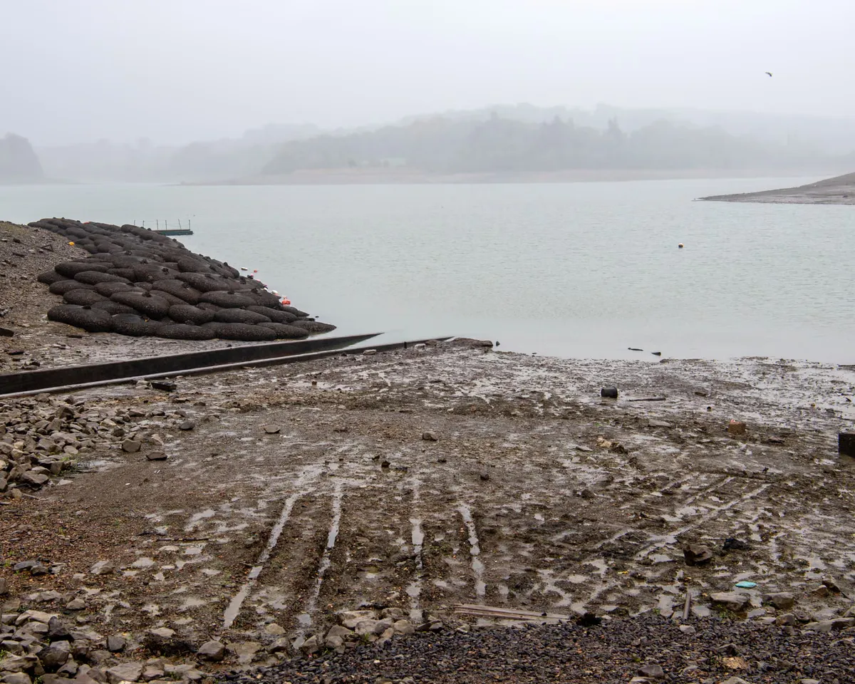 Görsel: The Guardian Environment Misty Ardingly reservoir shoreline with stacked sandbags and exposed muddy ground at low water — Görsel: The Guardian Environment