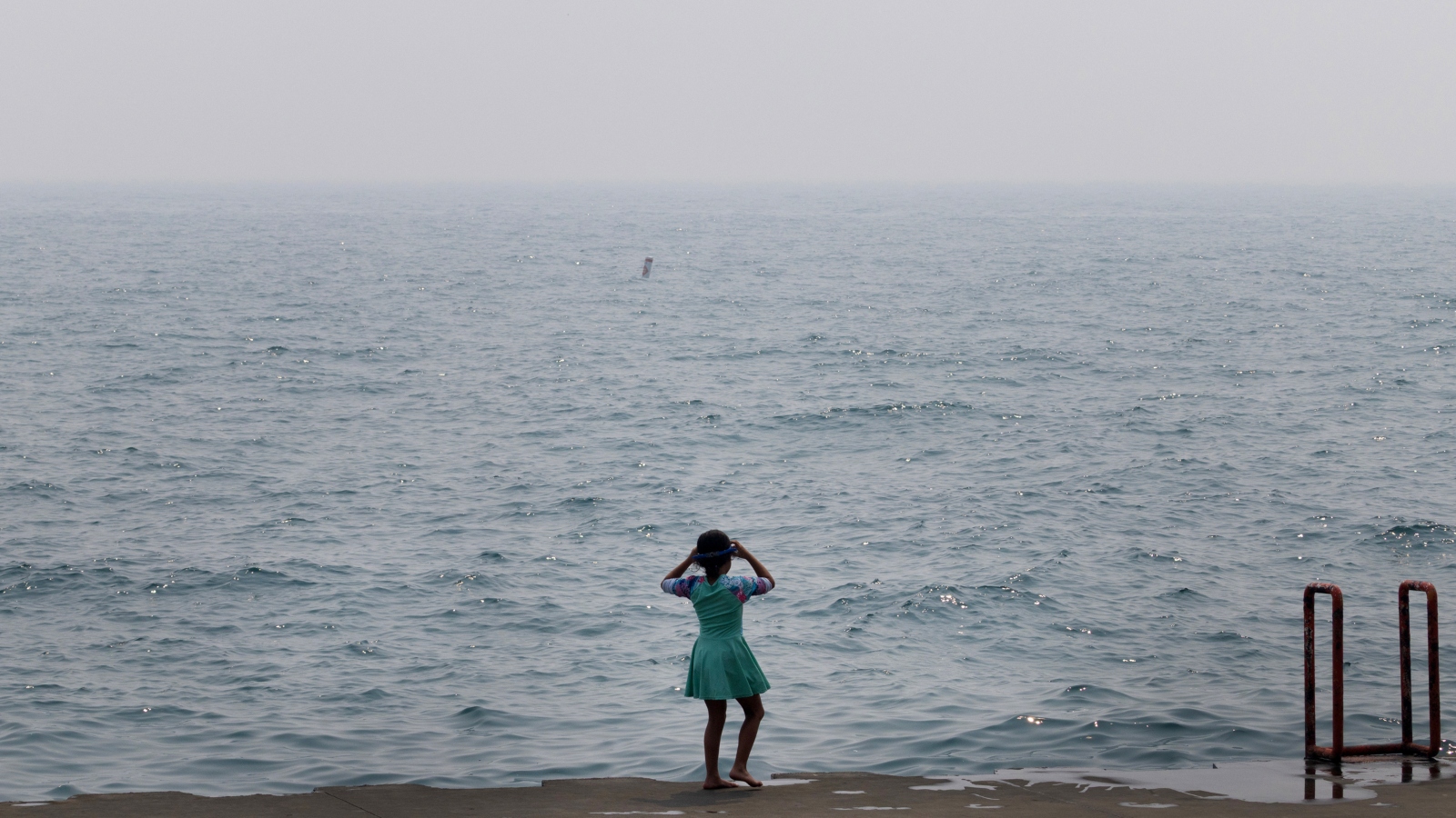 A child stands in front of a murky sea