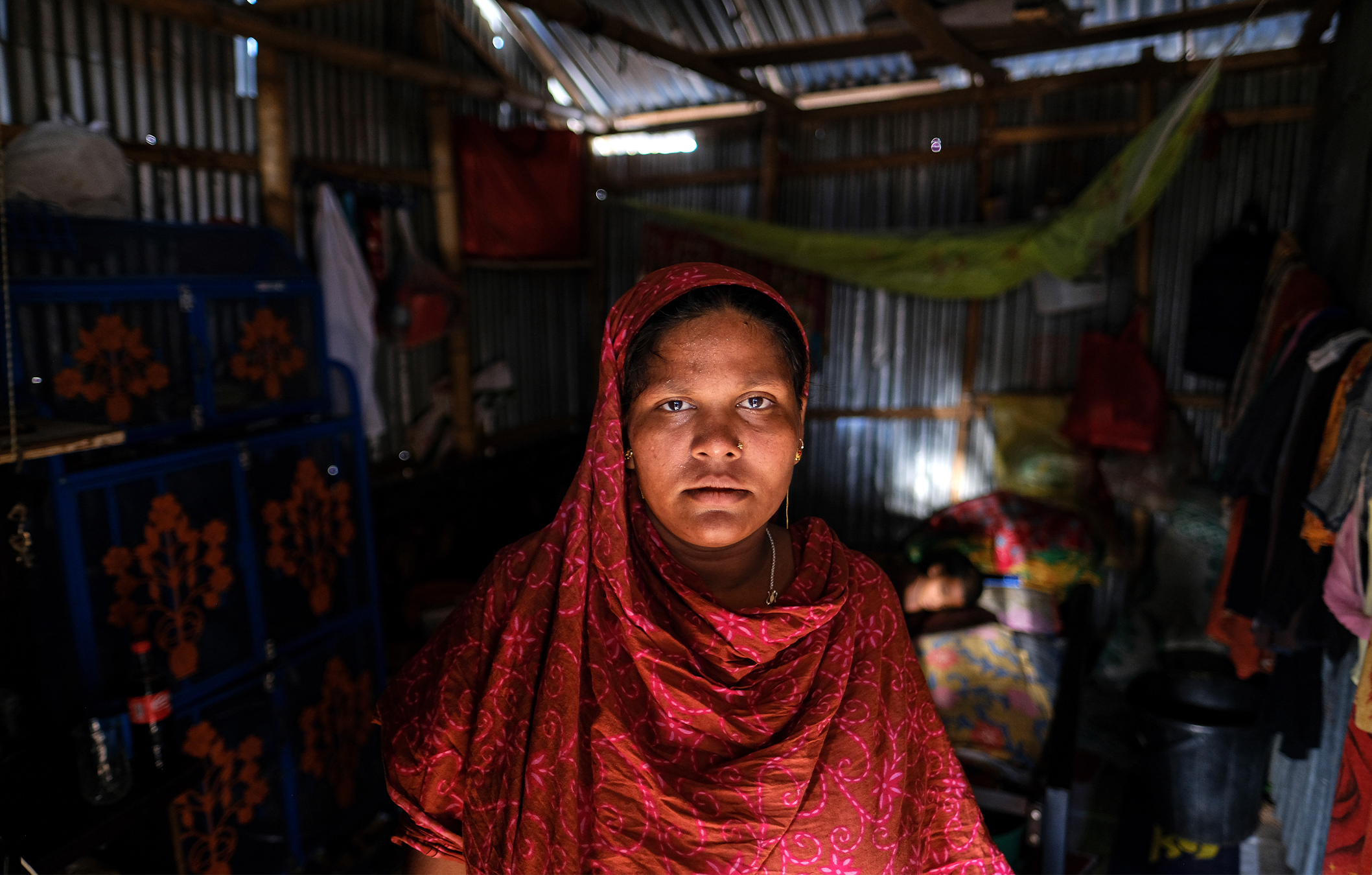 Arzu Begum stands by the door of her house in the poor Mirpur area of Dhaka in July, 2022. Begum's family was forced to flee their village in Bangladesh last year when the Meghna River flooded and destroyed their home. They moved to the capital, where they struggle to pay their rent and food bills on their small incomes. Image by AP Photo/Mahmud Hossain Opu.
