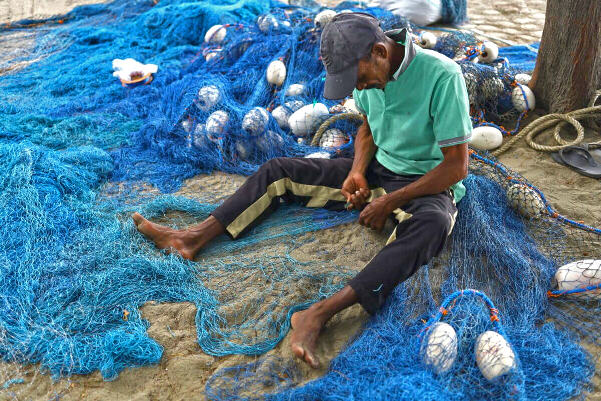 Efendi, an assistant to the panglima laot (customary fishery lead), mends a torn fishing net.