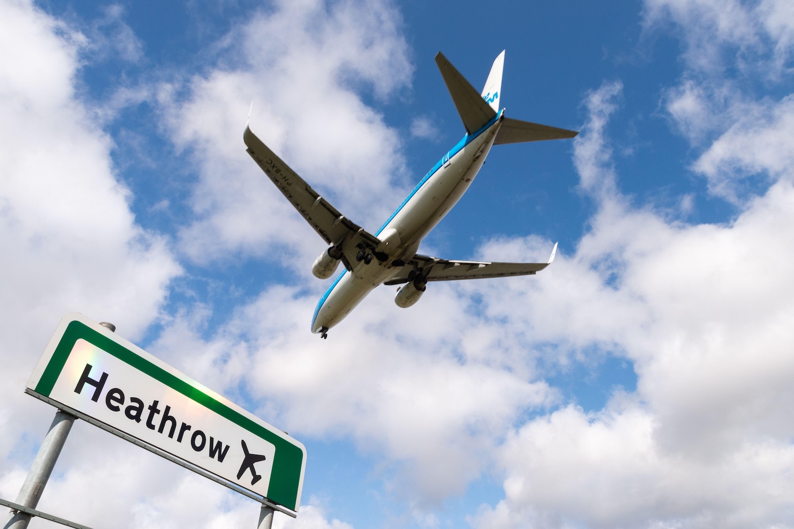 Plane flying over a road sign for Heathrow airport, London, UK. Credit: Avpics / Alamy Stock Photo