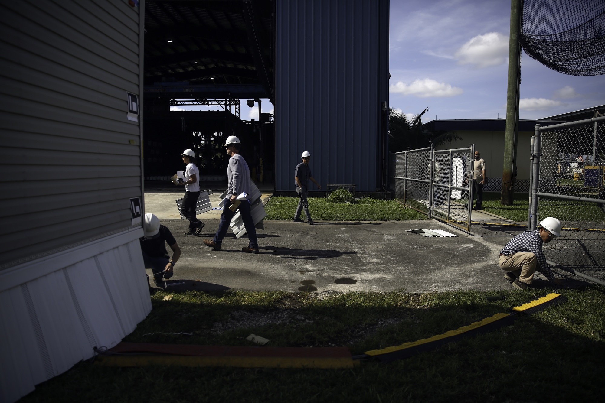 Image via Grist a group of people wearing hard hats walk around a corner near a wind testing site for manufactured housing — Image via Grist