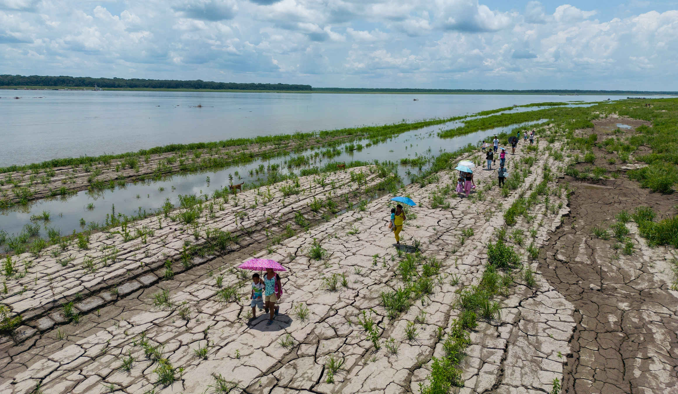 Indigenous people walk through a part of the Amazon River that shows signs of drought in Santa Sofia, on the outskirts of Leticia, Colombia, 2024. Image by AP Photo/Ivan Valencia.
