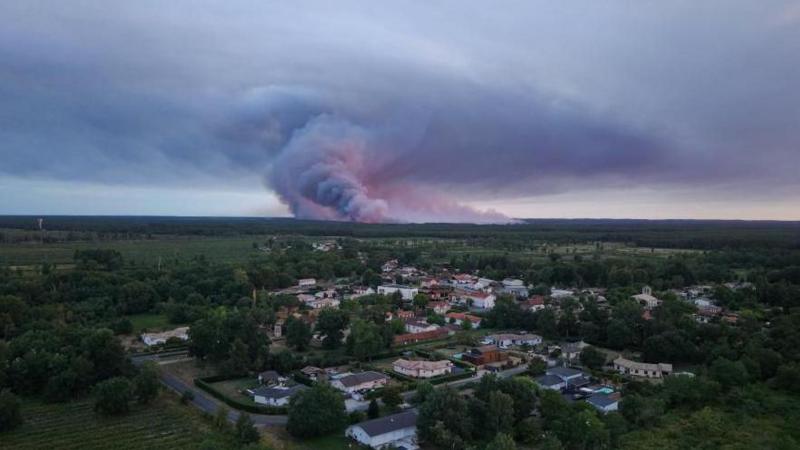 A done view showing the Sainte-Helene commune in France with smoke rising in the background during a wildfire in a forest area in Saumos
